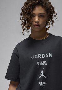 Black cotton t-shirt featuring "JORDAN" in white text, "QUALITY CLASSICS" below, and a silhouette of a jump man logo. Relaxed fit.