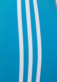 Top atlético turquesa con textura acanalada que presenta tres rayas blancas verticales en un lado, vista en primer plano que enfatiza el color y el diseño.