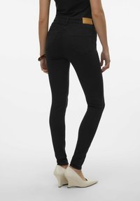 Jeans negros ajustados con una cintura alta, bolsillos traseros y un parche de cuero beige en la cinturilla; combinados con tacones puntiagudos color crema.