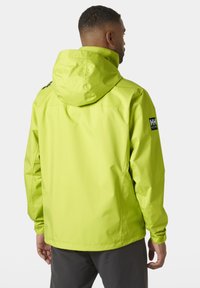 Chaqueta impermeable de un brillante color verde lima con capucha, presenta puños elásticos y un parche con el logo en el hombro izquierdo. Material suave y ligero.