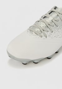 Chaussure de football en blanc et gris clair, dotée d'un dessus texturé, fermeture à lacets et crampons noirs pour une traction optimale. Détail d'accent dégradé pulvérisé.