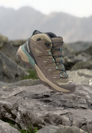 Chaussure de randonnée Salomon marron et verte avec étiquette Gore-Tex flottant au-dessus d'un terrain rocheux.