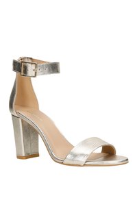 Metallisch zilveren hoge hak sandaal met een brede teband, enkelband met gesp sluiting en een vierkante blokhak. Soepele textuur.