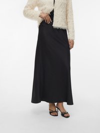 Saia preta maxi de cetim com acabamento suave, combinada com uma jaqueta texturizada de pele falsa creme e sandálias pretas com detalhe de laço.