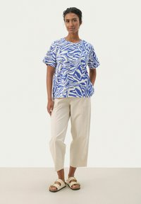 Haut à manches courtes bleu et blanc à motif, avec une coupe décontractée, associé à un pantalon large de couleur crème et des sandales beiges.