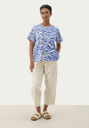 Haut à manches courtes bleu et blanc à motif, avec une coupe décontractée, associé à un pantalon large de couleur crème et des sandales beiges.