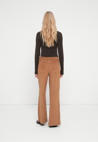 Brune faux suede flared bukser med baglomme, kombineret med en tætsiddende sort bluse med lange ærmer; glat tekstur og skræddersyet design.