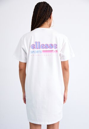 Osoba z długimi splecionymi warkoczami, nosząca duże kolczyki-koła oraz białą sukienkę-T-shirt z różowo-niebieskim logo "ellesse sports" na plecach.