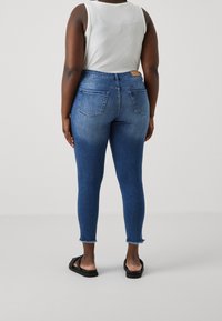 Slim jeans i mellanmörkblå denim med blekt mönster, fransig fåll, två bakfickor och slät yta.