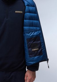 Marine fleece pullover met een kwart rits. Blauwe gewatteerde mouw heeft een zak met een drukknoop en een merklabel.