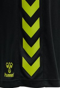 Svarta träningsshorts med djärva, limegröna chevronmönster längs sidan, med en liten gul logotyp av märket "hummel."