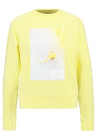 Sudadera amarilla de tejido suave, con una impresión gráfica frontal y un panel rectangular blanco con un logo en la parte inferior.
