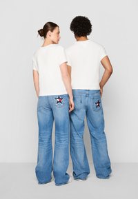 Hvite kortermede t-skjorter kombinert med lyseblå viddejeans som har stjerneformede lapper på baklommene.