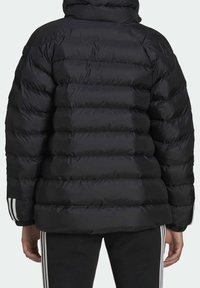 Doudoune noire matelassée avec sections cousues, col montant et poignets élastiques. Présente trois bandes blanches sur les manches. Texture lisse et brillante.