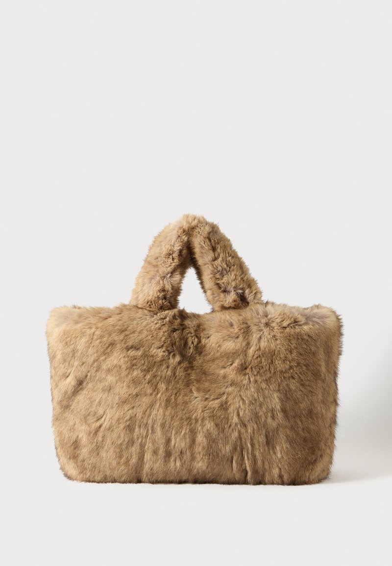 Sac à main en fausse fourrure tan, de forme rectangulaire, avec deux poignées supérieures, texture douce et motif de surface légèrement irrégulier.