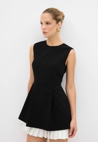 Robe noire sans manches avec un bustier ajusté et une jupe évasée plissée. Tissu lisse au design minimaliste, agrémenté de plis blancs en dessous.