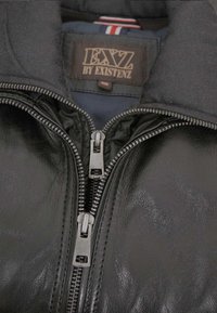 Schwarze Lederjacke mit hohem Kragen, Reißverschluss vorne und gewebten Texturdetails. Innen ist ein marineblaues Futter und ein sichtbares Markenlabel.