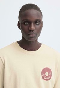 Beige sweatshirt met een ronde, rode vinylplaat afbeelding met de tekst "Blend." Zachte textuur en een ronde halslijn.