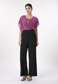 Gjennomsiktig lilla bluse med dekorative paljetter, kombinert med høytlivs svarte vidbente bukser og svarte sandaler med stropper.