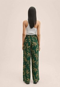 Green wide-leg pants with a gold leaf pattern, elastic waistband, and paired with a white tank top, viewed from the back.