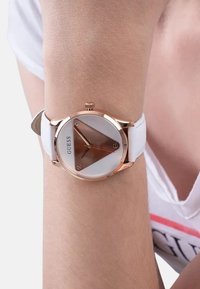 Ümar kell roosa kulla korpusega, valge kolmnurkne dial, ja valgest nahast rihm, millel on kolm roosa kulla käsku ja neli tunni tähist.