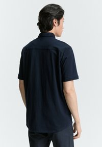 Marineblauwe korte mouwen shirt met een collsluiting, ontspannen pasvorm en een gladde textuur. Heeft een licht afgeronde zoom en opgerolde mouwen.