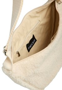 Bolso color crema con un exterior de textura suave, que cuenta con una apertura con cremallera, un bolsillo interior y una etiqueta de la marca en el forro.
