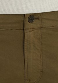 Pantalon kaki avec une texture lisse, doté d'un détail de bouton et d'une coupe droite. Couture d'accent le long des poches et de la ceinture.