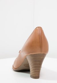 Escarpin en cuir marron à talon haut avec un bout pointu et un talon empilé texturé. Fini lisse avec des coutures décoratives le long du bord.