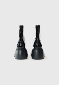 Pair of glossy black ankle boots with chunky platform soles viewed from the back on a plain white background.