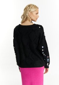 Maglione nero texturizzato con motivo a zigzag, caratterizzato da paillettes colorate sulle maniche. Abbinato a una gonna di maglia rosa.