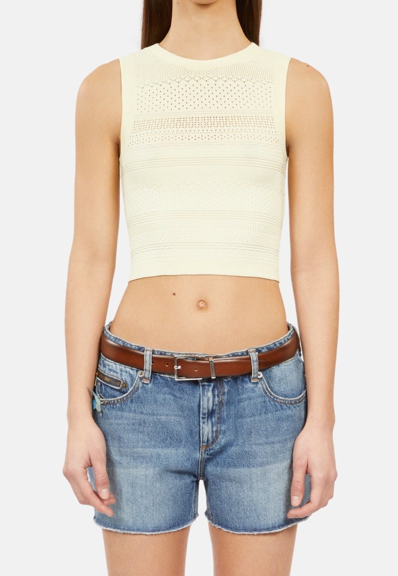 Haut court en maille jaune clair avec des motifs texturés, associé à un short en jean bleu et une ceinture en cuir marron.
