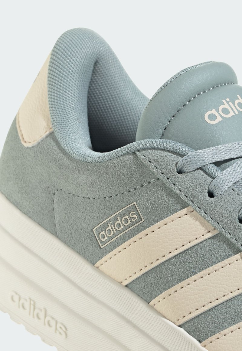 Light grey suede sneaker with cream leather stripes and accents. Features padded collar and logo on the side, textured lace area.