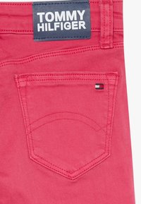 Tejido de mezclilla rosa con un bolsillo trasero cosido, que presenta una pequeña etiqueta de logotipo tricolor. La etiqueta dice "TOMMY HILFIGER" en un texto en negrita de color blanco.
