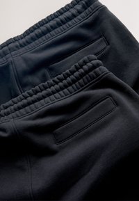 Gros plan sur un pantalon de jogging noir montrant une ceinture élastique et des poches arrière avec des ouvertures horizontales.