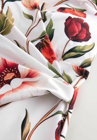 Kangas bunga dengan bunga merah dan merah muda besar serta daun hijau di latar belakang putih, memperlihatkan tekstur yang halus dan lembut serta lipatan yang elegan.