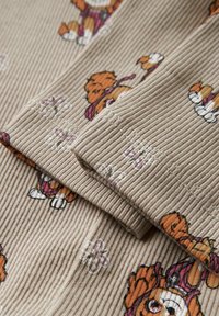 Beżowa dzianina prążkowana z kolorowymi wzorami niedźwiedzi i kwiatów. Tkanina ma miękką fakturę, z widocznymi szwami na krawędziach.