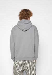 Sweat à capuche gris avec une texture douce et une capuche spacieuse, doté de poignets et d'un ourlet côtelés. Porté avec un pantalon à carreaux.
