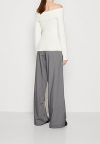 Maglione bianco con spalle scoperte abbinato a pantaloni ampi grigi e morbidi. Il tessuto ha una consistenza soffice, con una silhouette rilassata.