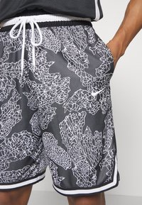 Shorts noirs avec un motif abstrait craqué blanc, taille élastique avec cordon de serrage, poche latérale et bord contrastant blanc.