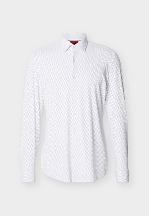 Valge pika varrukaga nööpidega särgi väikese musta täpikese mustriga ja terava kraega, eksponeeritud lihtsal heledal taustal.