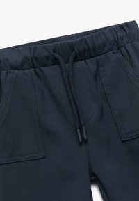 Pantalones azul marino con cintura elástica y cordón, dos bolsillos delanteros y una tela suave y texturizada.