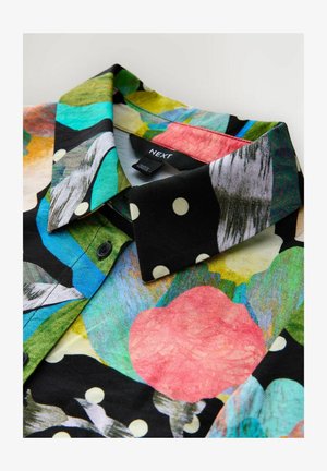 Collared shirt with black, white polka dots and colorful abstract floral patterns, featuring a visible "NEXT" brand label.