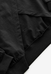 Svart bomullströja med lagerdesign, ribbade ärmslut och en texturerad insida med broderad detalj.