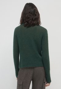 Waldgrüner Strickpullover mit langen Ärmeln, strukturiertem Finish und lockerer Passform. Taillenlänge mit einem dezenten gerippten Ausschnitt.