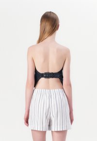 Denim avskåret topp med åpen rygg og justerbart utstyr, parret med hvite stripete shorts med snøring i en avslappet passform.