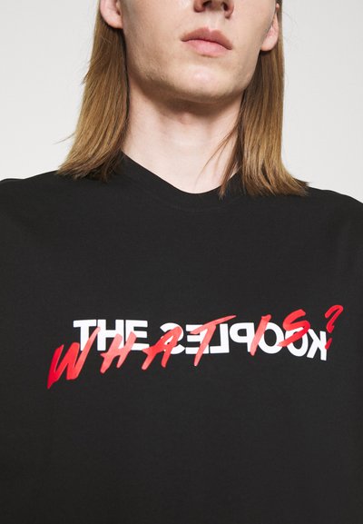 Schwarzes Baumwoll-T-Shirt mit Rundhalsausschnitt, auf dem Vorderteil prominent mit weißem und rotem Text: "DIE SAMMLER WAS IST?" bedruckt.