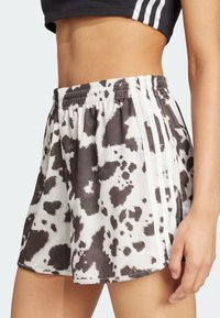 Barevné šortky s černobílým designem kravího vzoru, s elastickým pasem a bílými bočními proužky. Světlá, hladká textilie.
