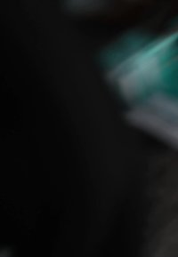 Abstraktný pohľad na zelenkavé odtiene, ktoré sa spájajú s tmavými povrchmi; obsahuje rozmazané tvary, ktoré naznačujú hladkú textúru a postupné prechody.