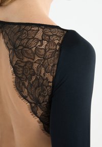 Body nero con dettaglio posteriore in pizzo floreale, caratterizzato da una texture semi-trasparente, design elegante e cuciture a contrasto lungo i bordi.